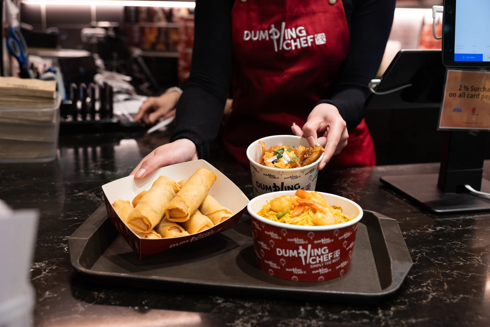 A Dumpling Chef team member arranging freshly prepared meals on a tray at the counter